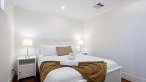 A neatly arranged hotel room with a large bed, two bedside tables, and a ceiling vent. - Hidden Gem - Fremantle Apartment (Fremantle)
