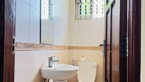 Ein kleines Badezimmer mit einem weißen Waschbecken, einer Toilette und einem Fenster mit dekorativen Gitterstäben.