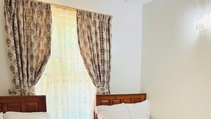 Ein Hotelzimmer mit zwei hölzernen Betten, einem Nachttisch und einem Fenster mit gemusterten Vorhängen.