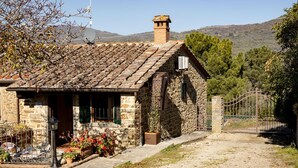 Un bâtiment en pierre avec un toit en tuiles, un petit porche doté de sièges extérieurs et un portail.