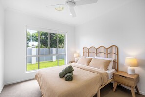 A bedroom with a large window, a bed with a wooden headboard, two bedside lamps, and a ceiling fan. - Mooloolaba Parkway Palms Retreat | Spacious 3BR with Patio & BBQ | Pet-Friendly (Mooloolaba)