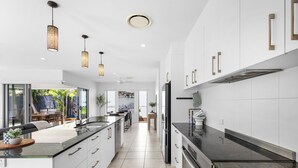 A modern kitchen with white cabinets, black countertops, and pendant lighting. - Mooloolaba Parkway Palms Retreat | Spacious 3BR with Patio & BBQ | Pet-Friendly (Mooloolaba)