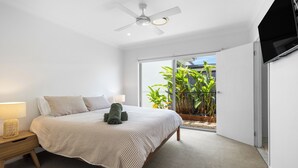 A bedroom with a bed, bedside table, lamp, ceiling fan, and a view of a balcony with plants. - Mooloolaba Parkway Palms Retreat | Spacious 3BR with Patio & BBQ | Pet-Friendly (Mooloolaba)