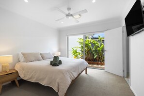 A bedroom with a bed, bedside table, lamp, ceiling fan, and a view of a balcony with plants. - Mooloolaba Parkway Palms Retreat | Spacious 3BR with Patio & BBQ | Pet-Friendly (Mooloolaba)