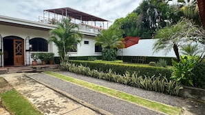 A two-story house with a covered balcony, a well-maintained garden with hedges and plants, and a gravel pathway. - Hotel Vizcaino Leon (Leon)