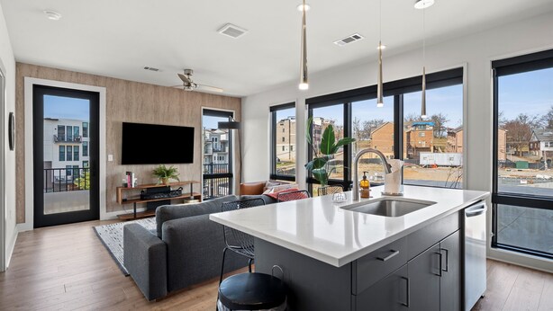 A modern kitchen with a large island, a dining area with a sofa, and a TV mounted on the wall. - Odyssey | Modern 2BR Family Retreat Near Downtown (Nashville)