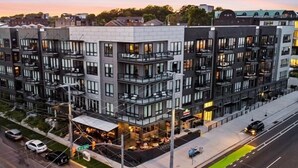 A modern multi-story building with balconies, a restaurant on the ground floor, and a green bike lane. - Odyssey | Modern 2BR Family Retreat Near Downtown (Nashville)