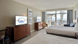 Ein Hotelzimmer mit Bett, Fernseher, Schminktisch, Stuhl und einem Balkon mit Meerblick.