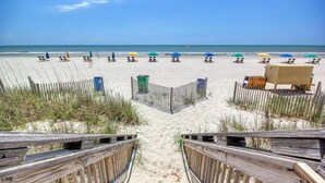 Ein Strand mit Holzstegen, die zu Liegestühlen und Sonnenschirmen führen.