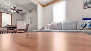 A modern living room with a wooden dining table, a gray sofa with patterned cushions, a ceiling fan, and a window with blinds. - Farmhouse less than a mile from beaches (Millcreek Township)