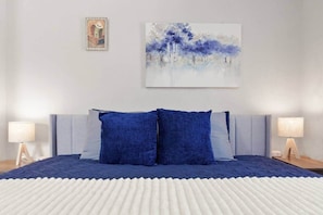 Un dormitorio con cama, dos lámparas de noche, un cuadro enmarcado y un cuadro abstracto grande en la pared.