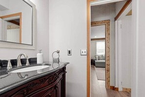 Un baño con lavamanos de mármol, un espejo grande y armarios de madera.