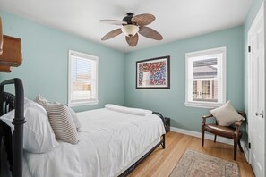 A bedroom with a bed, a chair, a ceiling fan, and two windows with blinds.