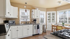 Une cuisine moderne avec des meubles blancs, un four à micro-ondes encastré, des appareils en acier inoxydable et un coin repas comprenant une table et des chaises.