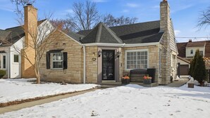 Une maison en pierre avec une porte noire, une cheminée et une allée recouverte de neige.