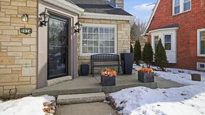 Une maison en pierre avec une porte noire, un banc et des jardinières remplies de fleurs sur le porche.