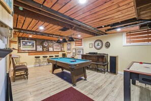 A recreational room with a pool table, bar stools, and a ping pong table.