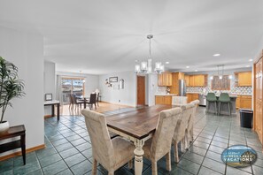 A spacious kitchen with wooden cabinets, a dining area with a large wooden table and chairs, and a view of the dining area through a glass door.