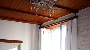 Un dormitorio con techo de madera, una cama con colcha floral, un radiador, un perchero para toallas y una ventana con cortinas.