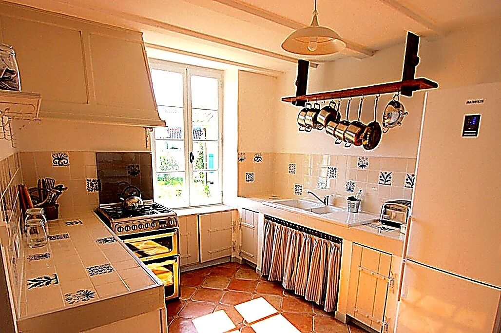 A kitchen with a stove, sink, and hanging pots. There is a window providing natural light.