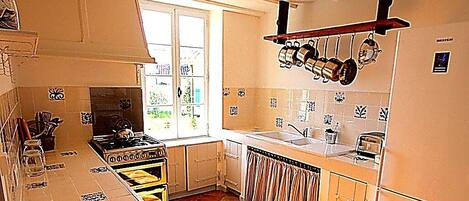 A kitchen with a stove, sink, and hanging pots. There is a window providing natural light.