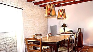 Un comedor con una mesa y sillas de madera, luces colgantes y una pared blanca.