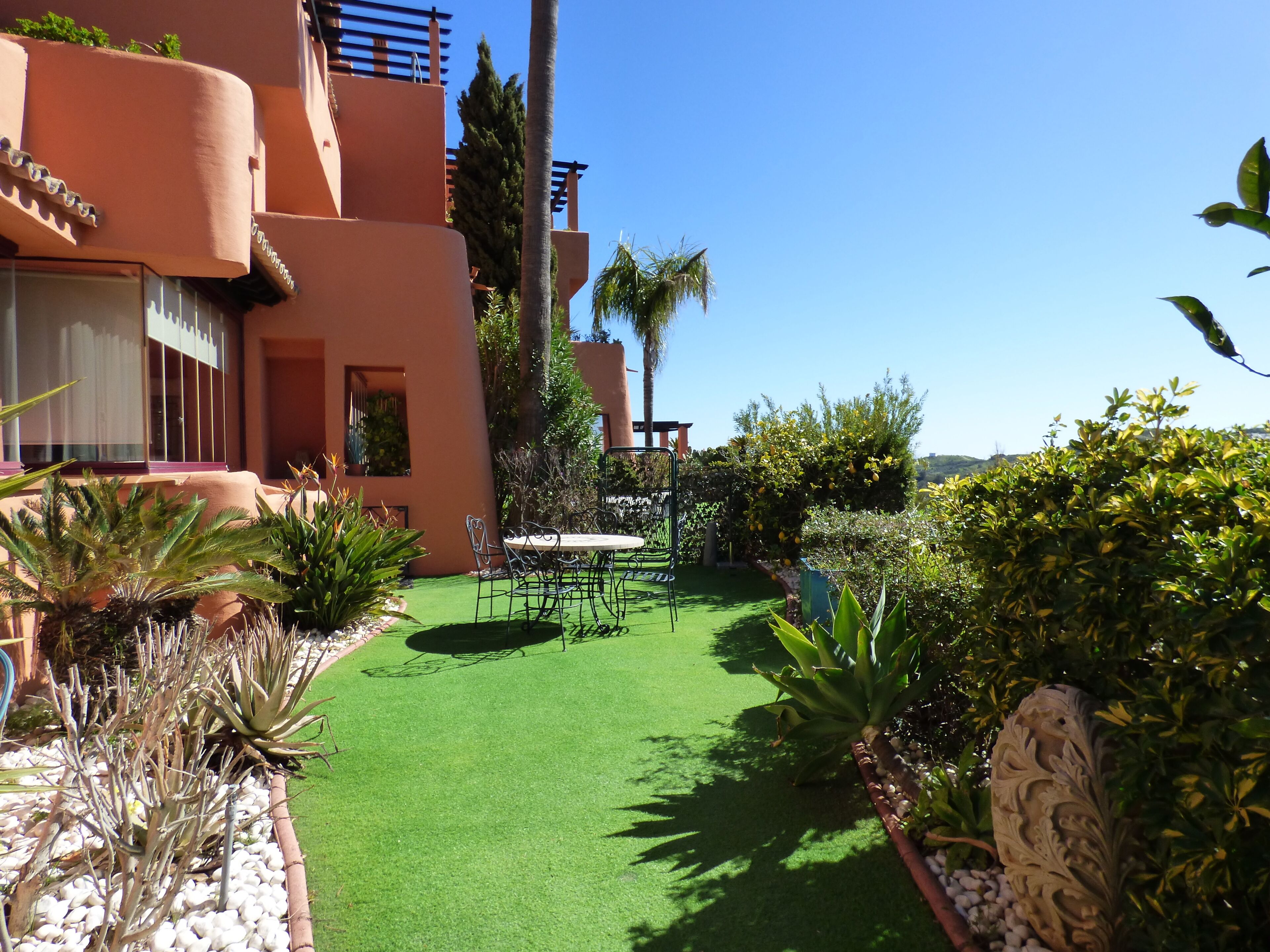 A courtyard with artificial green turf, palm trees, and various plants.