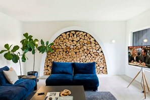 A modern living room with a blue sofa, a coffee table, and a fireplace with stacked logs. - Elegant Home | Hot Tub & Fire Pit | Bocce Ball (Whitefish)