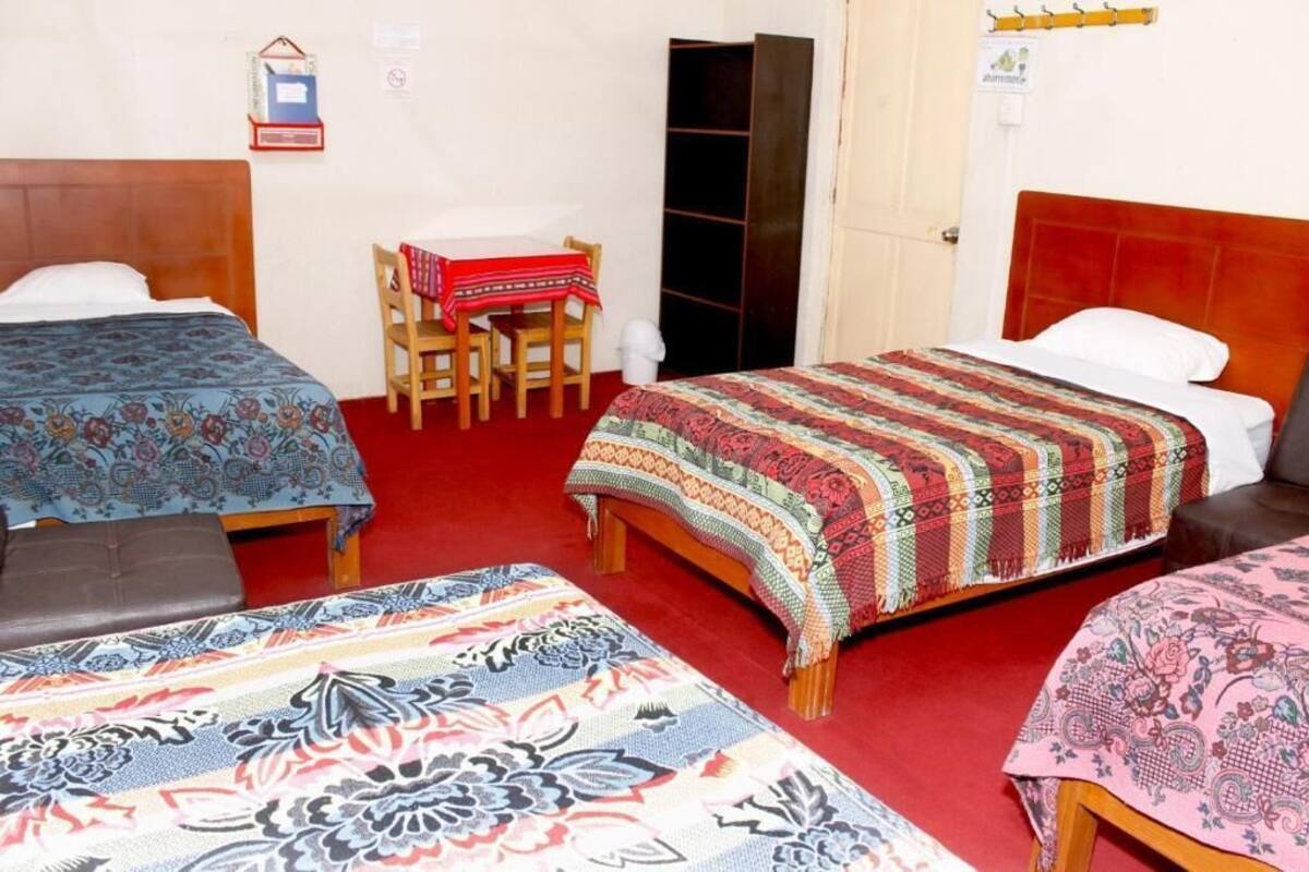 A room with three beds, a wooden chair, a small table with a red tablecloth, and a wardrobe.