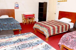 Une pièce avec trois lits, une chaise en bois, une petite table recouverte d’une nappe rouge et une armoire.