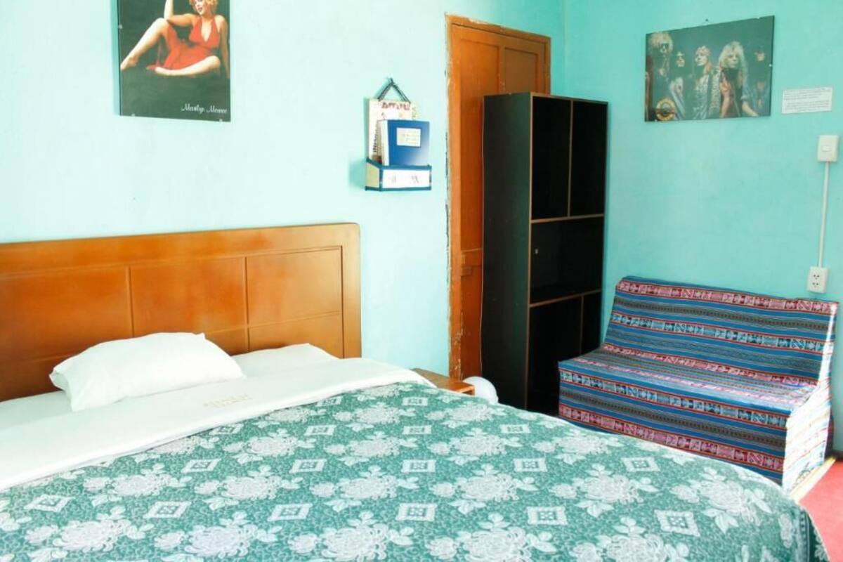 A bedroom with a bed, a wooden headboard, a patterned bedspread, a colorful sofa, a wardrobe, and wall decorations.