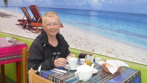 Eine Person sitzt an einem Tisch mit Frühstücksangeboten, im Hintergrund ist eine Strandmalerei zu sehen und ein Sessel mit Kissen.