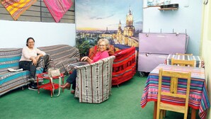 Ein Zimmer mit grünem Teppich, zwei Sofas, einem roten Sessel, einem violetten Schrank und einem Tisch mit gestreiftem Tischläufer.