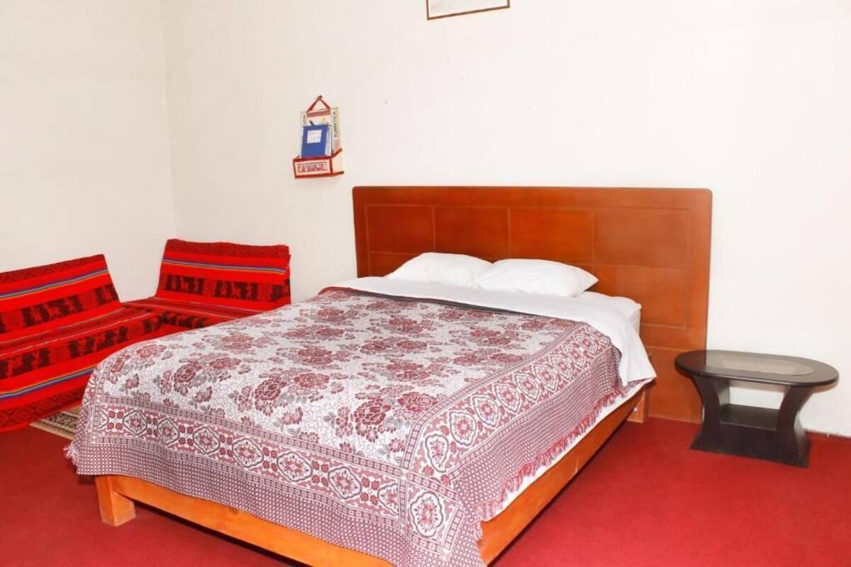 A room with a bed, a red and white patterned bedspread, a red and white patterned pillow, and a small black table.