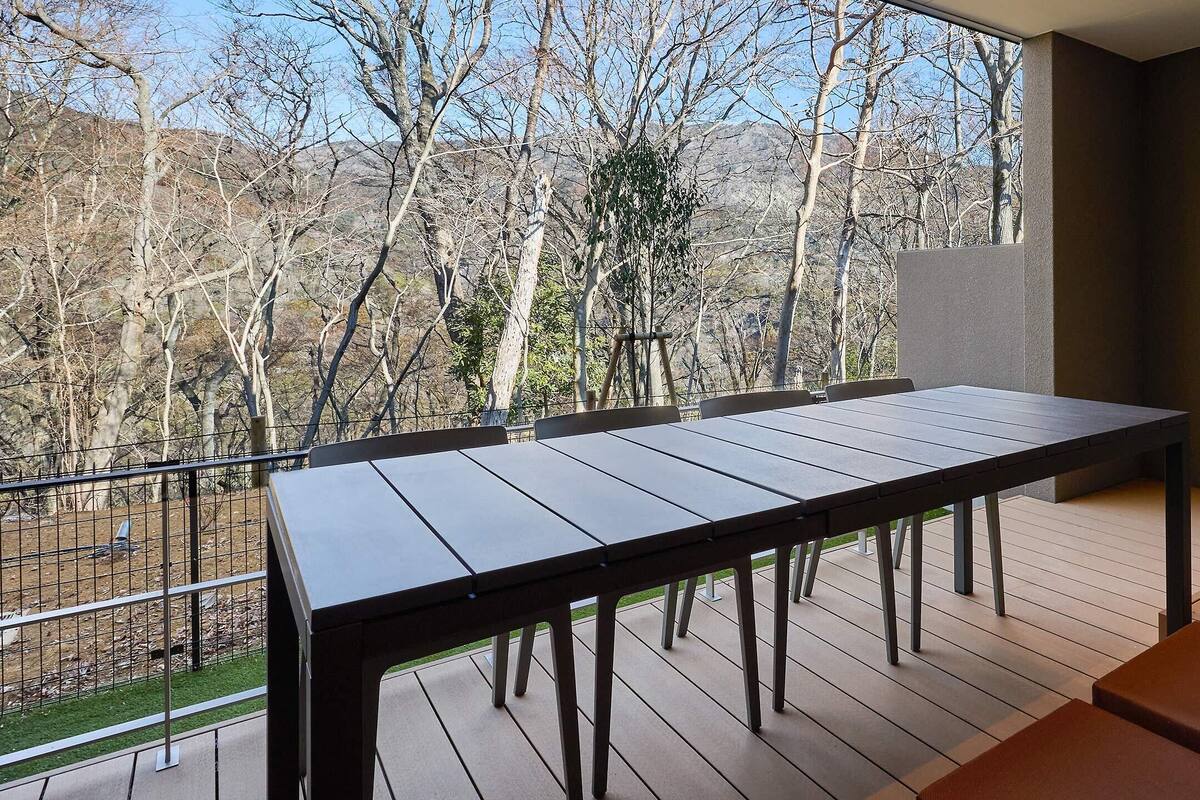 A balcony with a table and chairs, a view of trees and hills, and a power outlet on the wall.