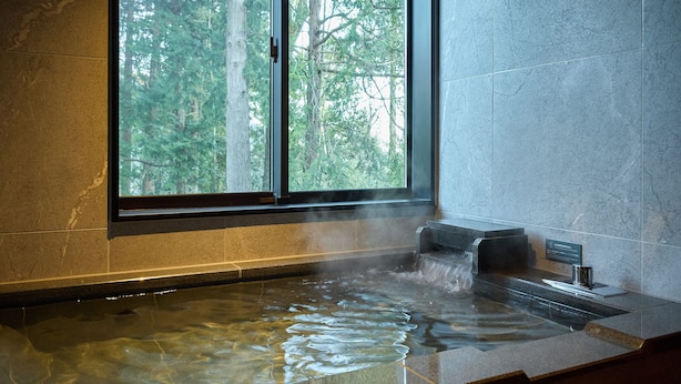 A hot tub with a view of a forest through a window.