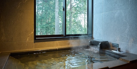 A hot tub with a view of a forest through a window.