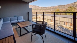 Un balcone con un divano, un tavolo e una sedia, con vista su un’area di parcheggio e edifici sullo sfondo di montagne.