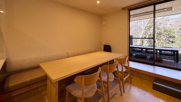 Una habitación con una larga mesa de madera, cuatro sillas, un banco y un ventanal con vistas a una zona de estar al aire libre.