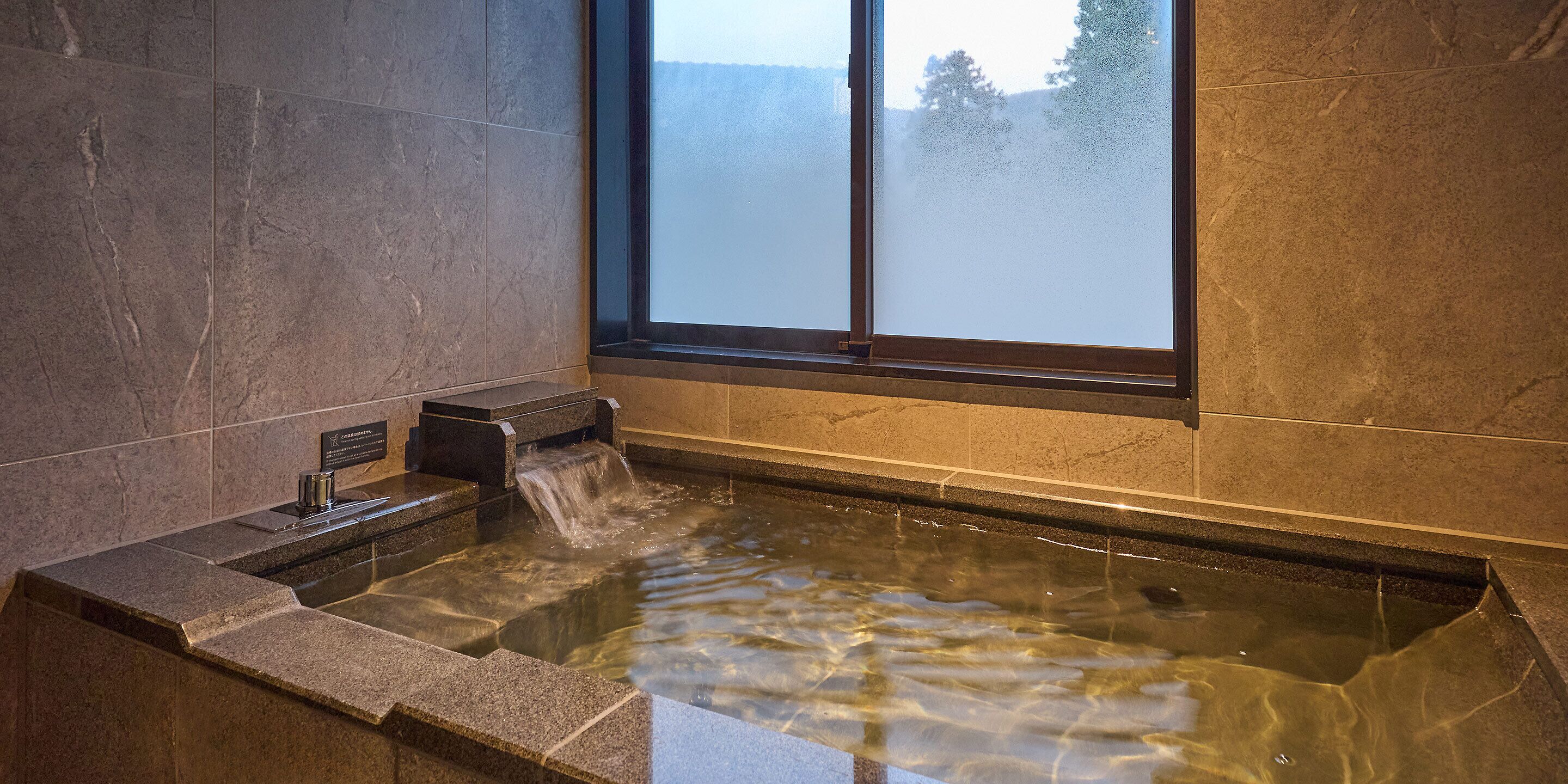 Un espacio de spa con un jacuzzi, una ventana con vidrio satinado y una pared de piedra.
