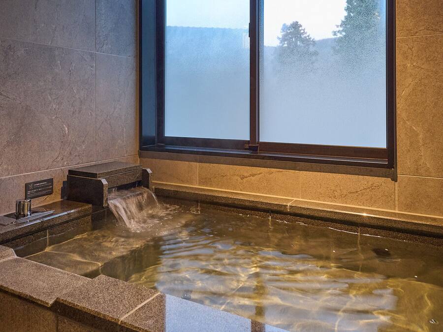 Un espacio de spa con un jacuzzi, una ventana con vidrio satinado y una pared de piedra.