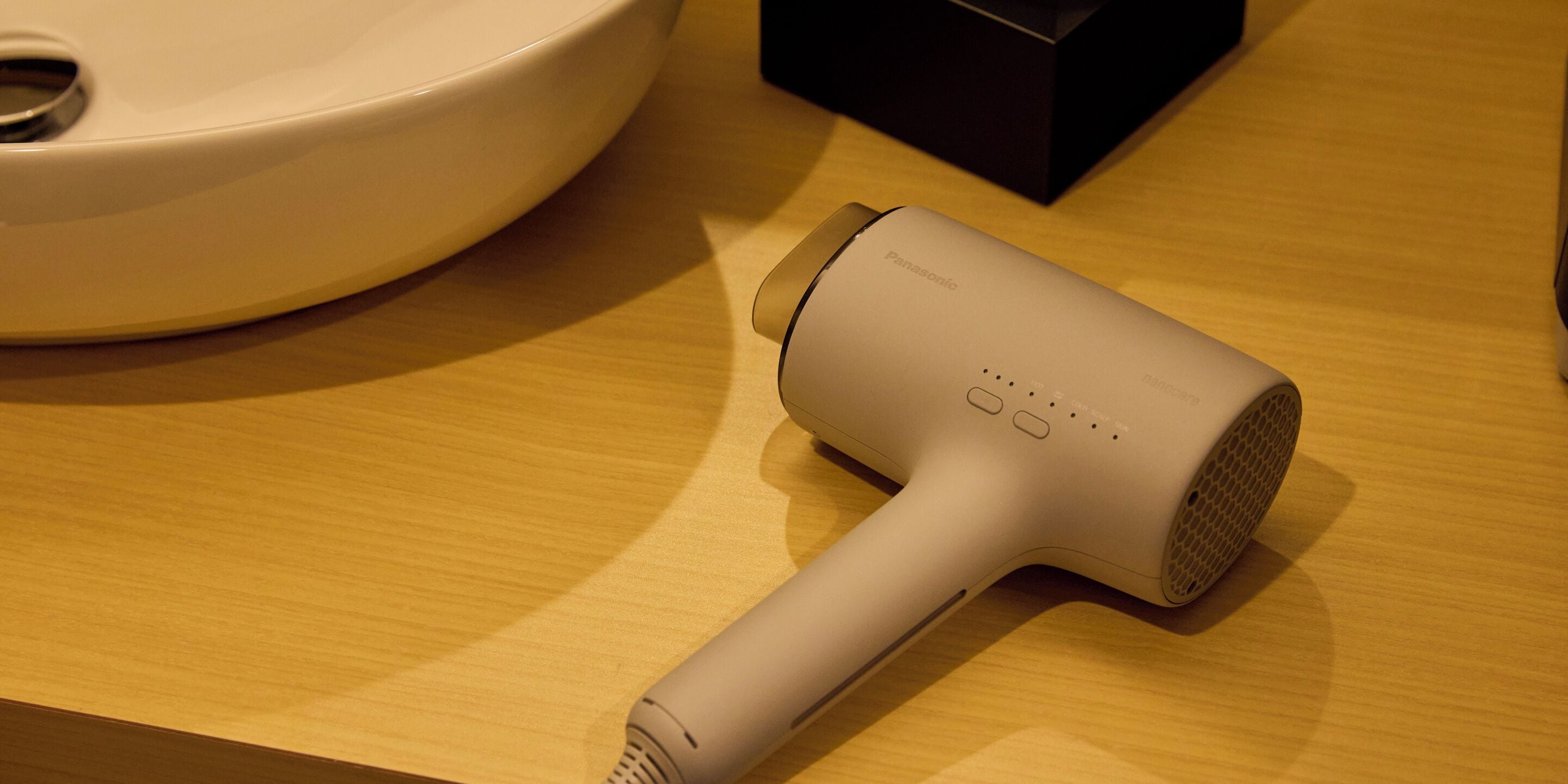 A bathroom with a white sink, a beige hair dryer, and a black box on the countertop.
