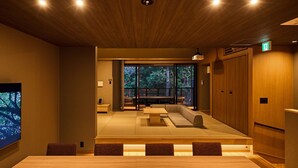 A modern interior with a wooden ceiling, a large table with chairs, a sofa, and a view through large windows.