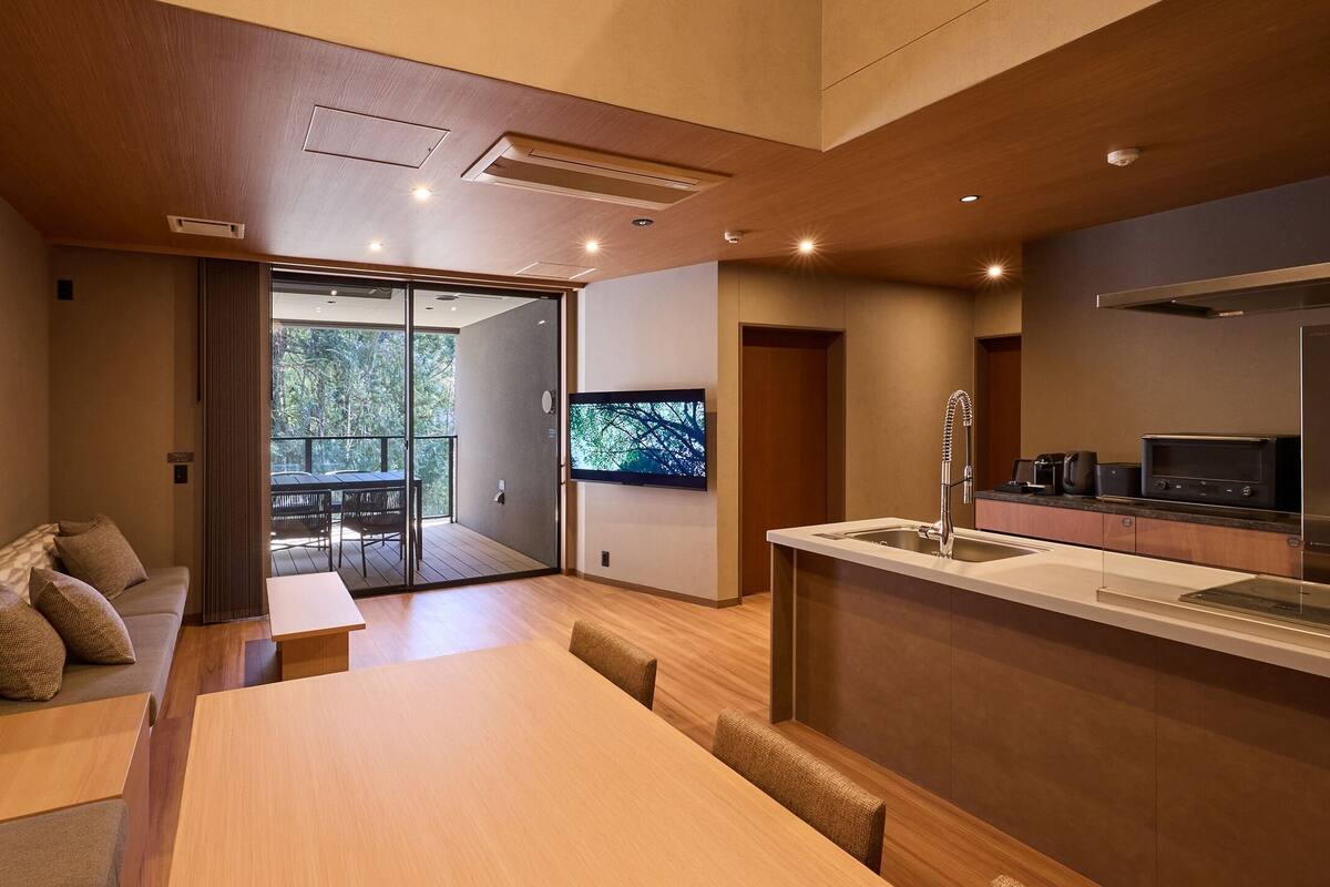 A modern kitchen with a built-in stove, a dining area with a wooden table and chairs, and a sliding glass door leading to an outdoor patio.