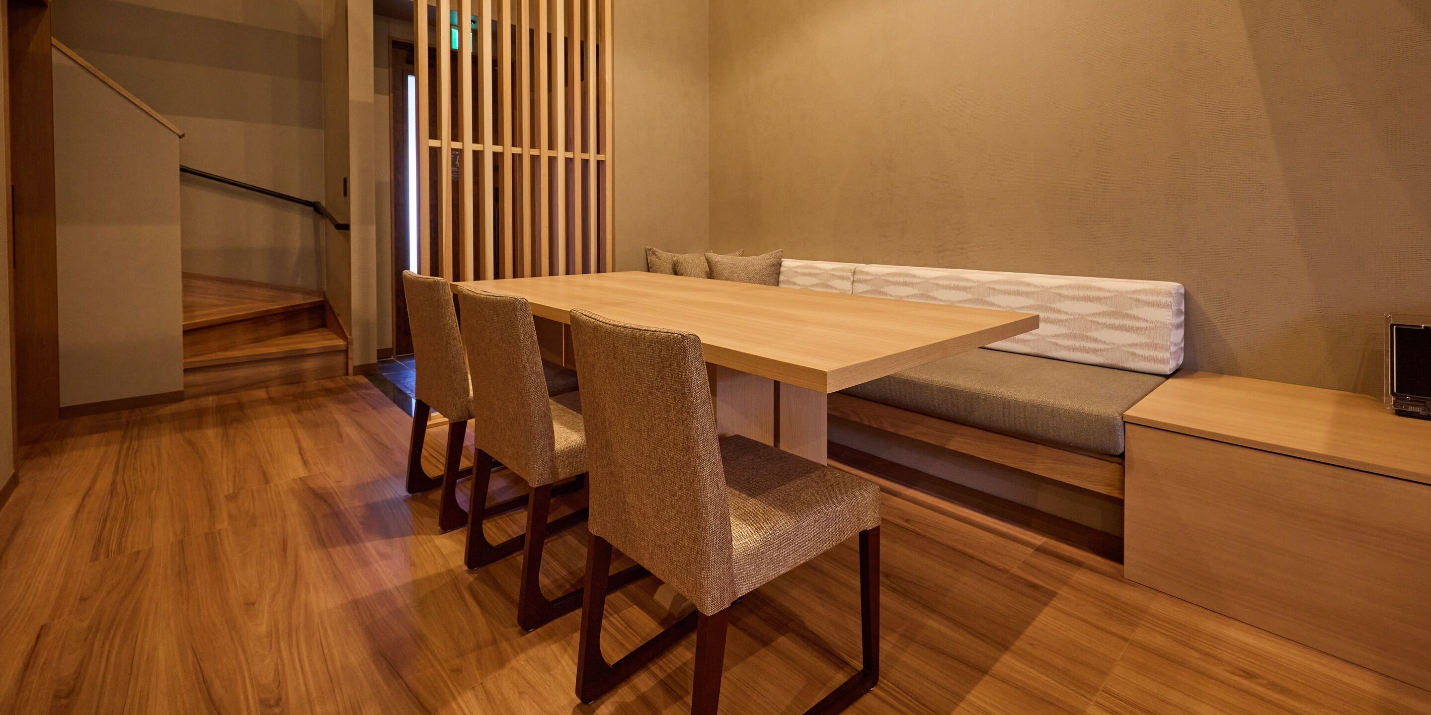 A modern interior with a wooden dining table, four chairs, a bench, and a staircase.