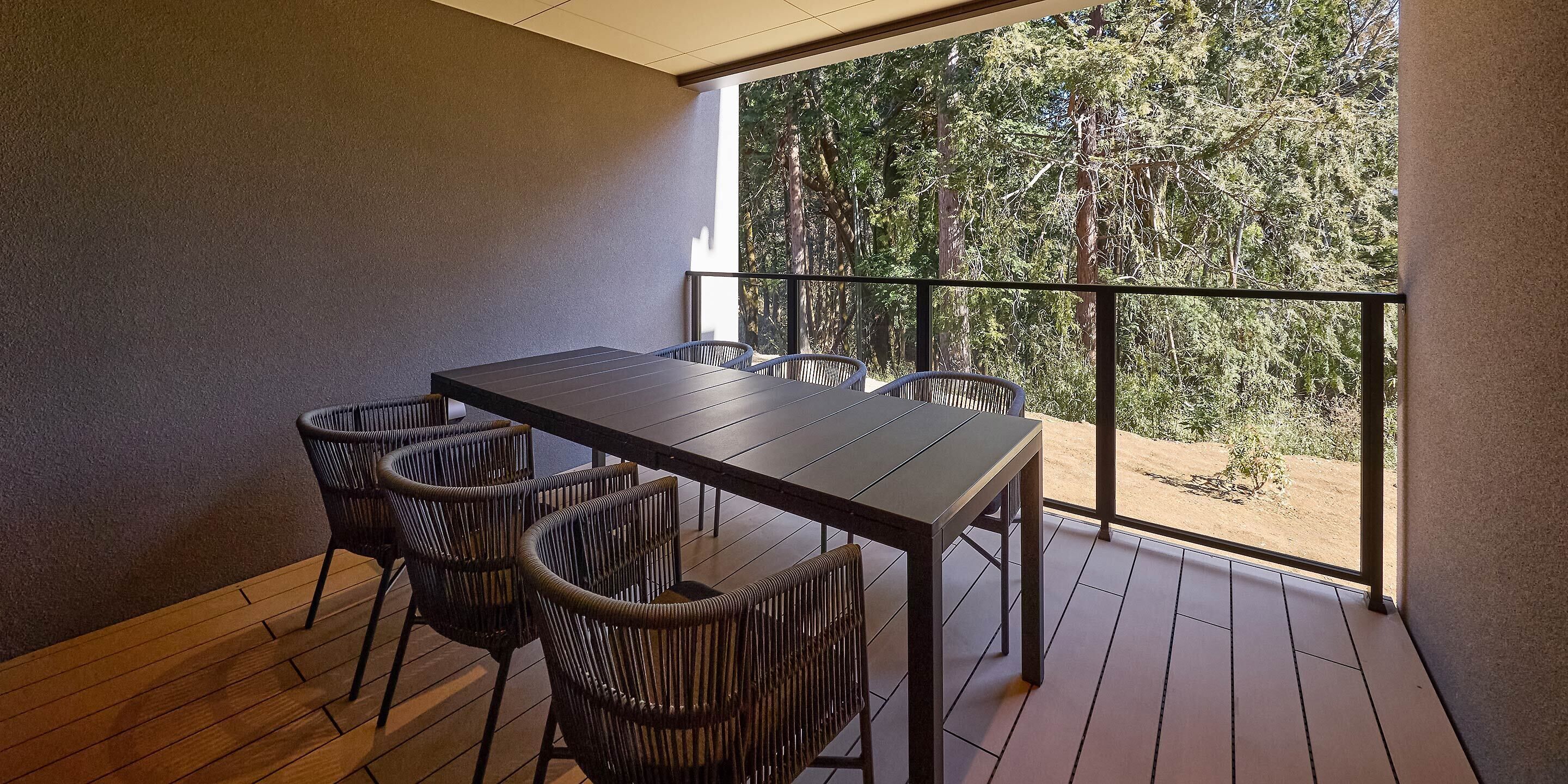 A balcony with a table and chairs, a view of trees, and a wooden floor.