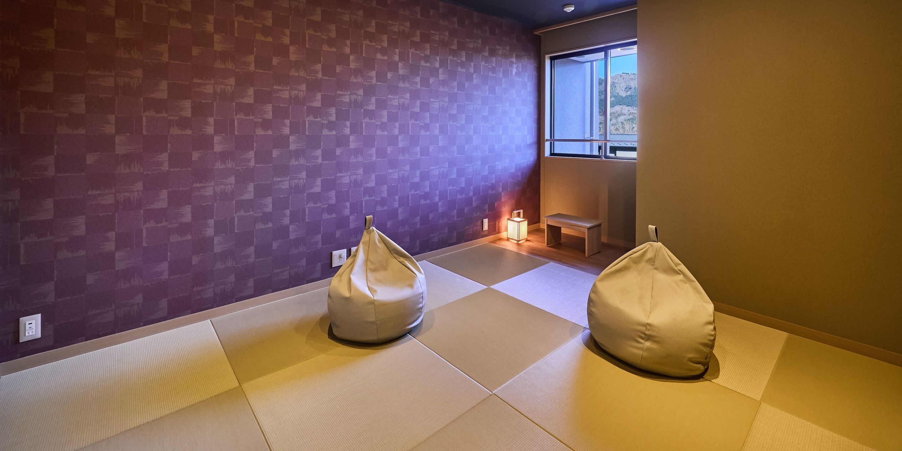 A room with tatami mats, two bean bags, a small table, and a window with a view.