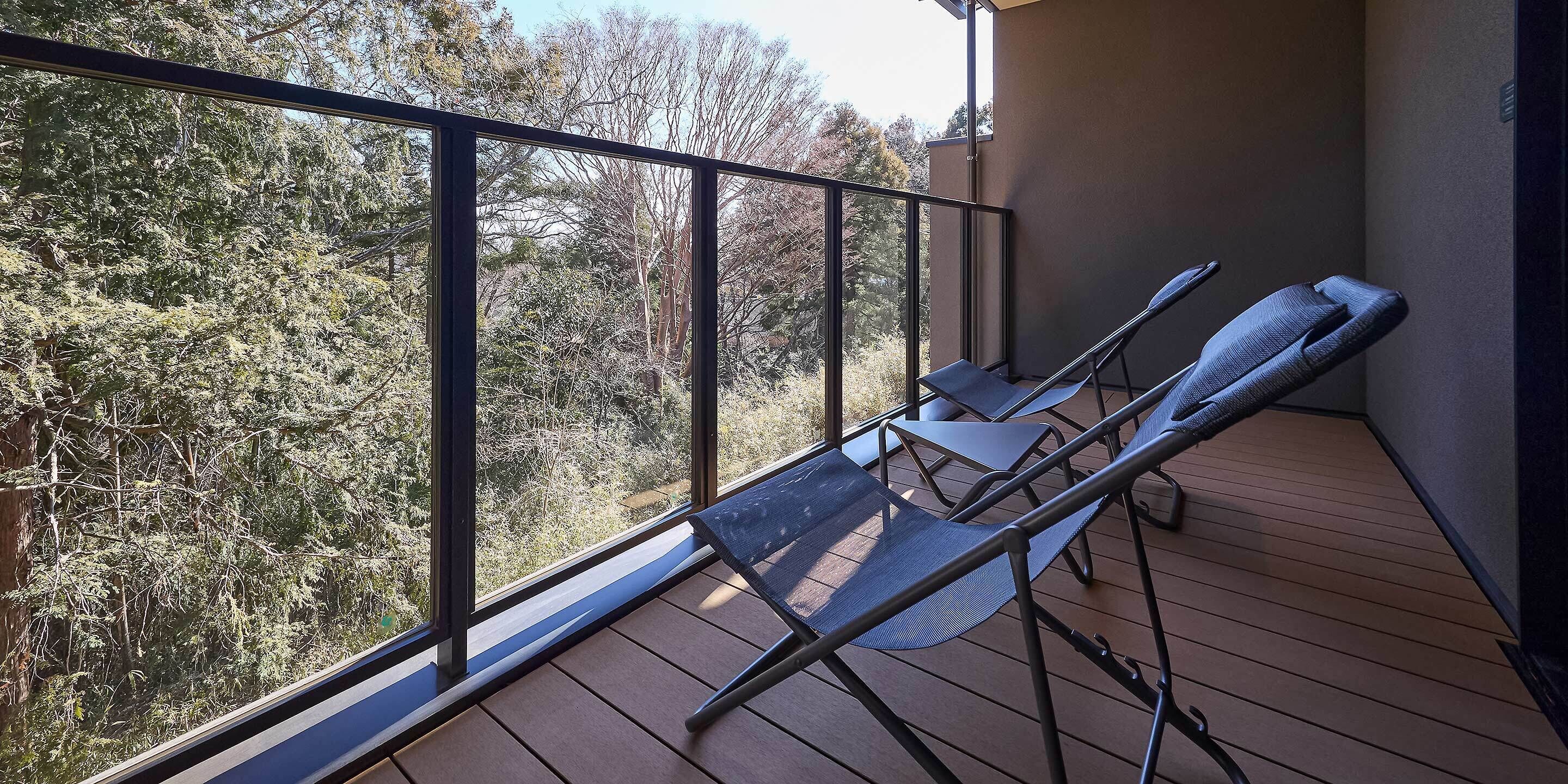 A balcony with two lounge chairs, a wooden floor, and a view of trees.