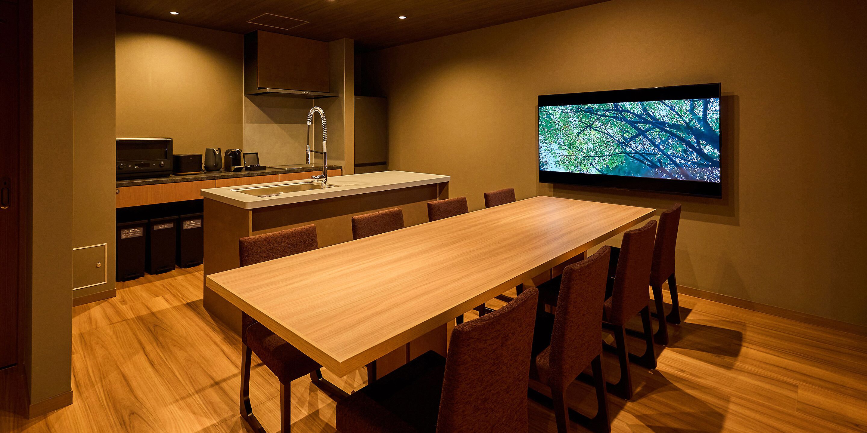 A modern kitchen with a wooden table and chairs, a flat-screen TV, and a built-in oven.