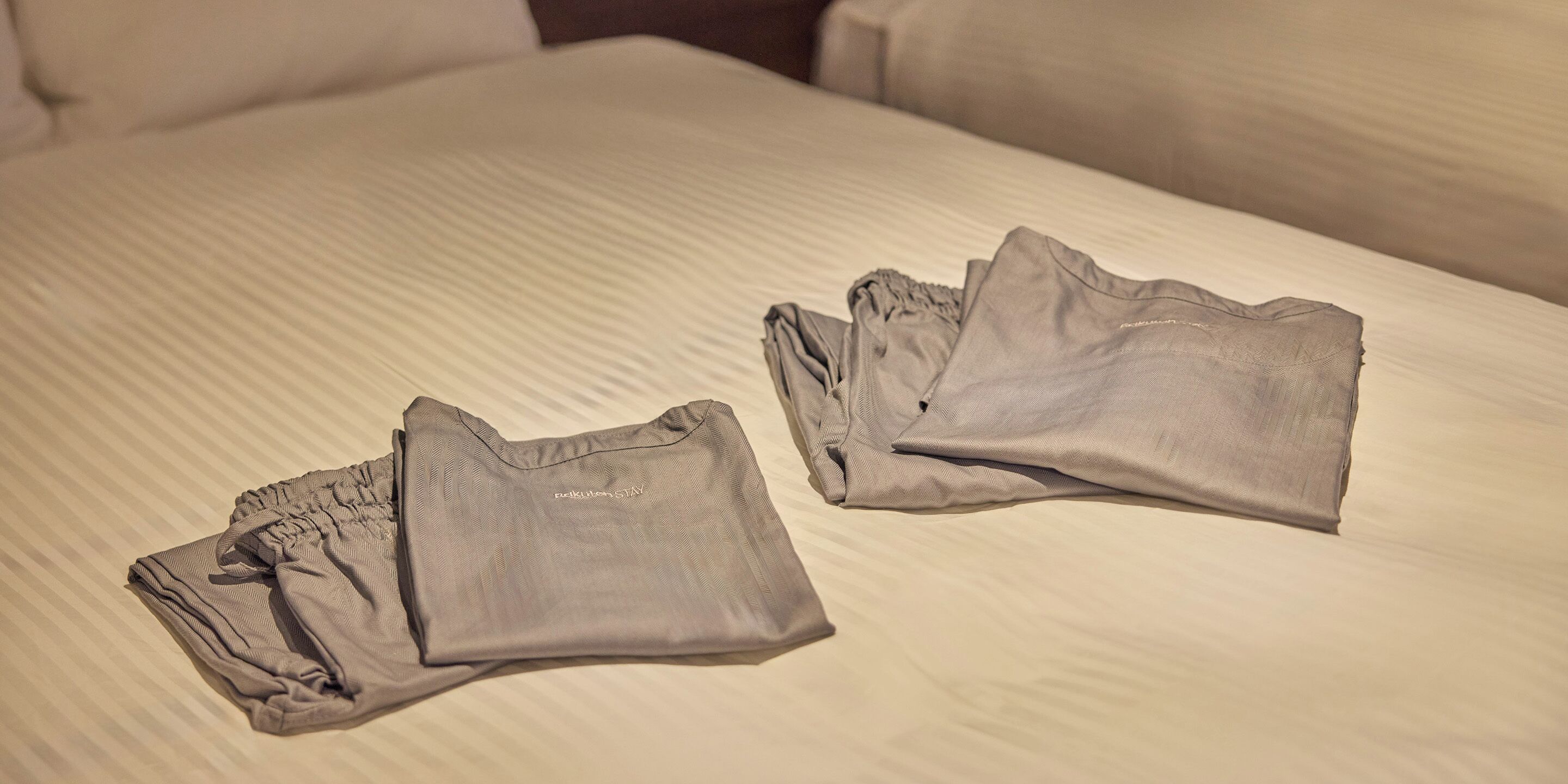Un lit recouvert d’une couverture à rayures, avec deux chemises grises pliées posées dessus.